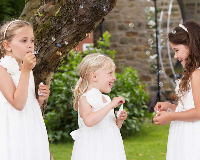 Dre Mädchen in weißen Kleidern stehen in einem Garten und pusten Seifenblasen