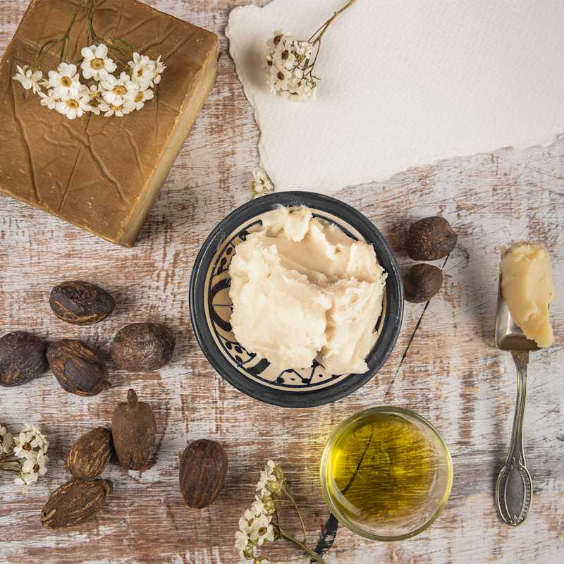 Sheabutter in einer dekorierten Schale, daneben liegen Früchte des Karitébaums