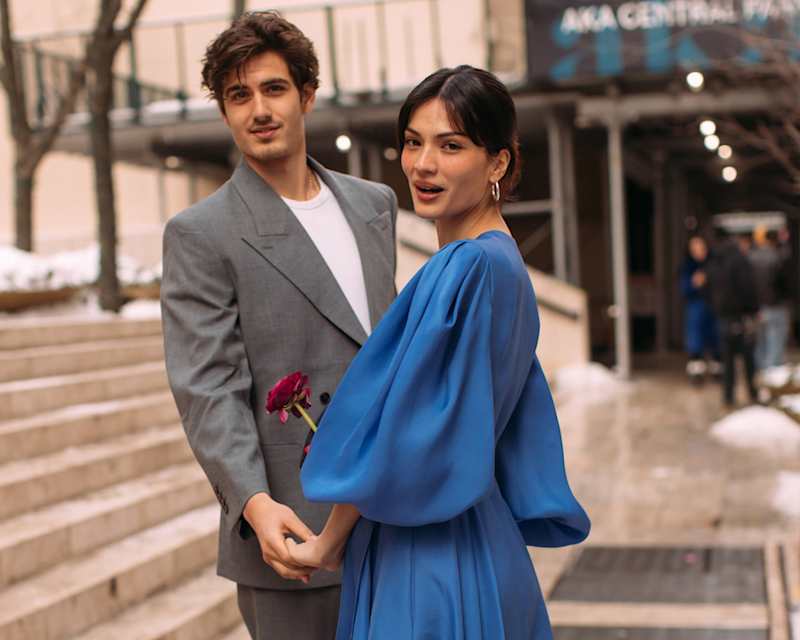 Ein Mann im grauen Anzug und eine Frau in einem blauen Kleid halten sich an den Händen