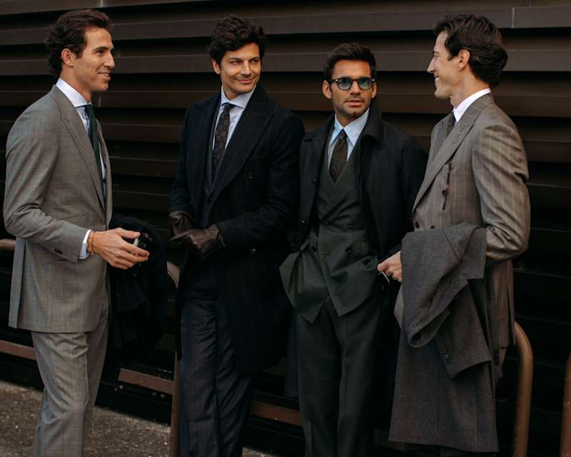 Vier Männer stehen im Halbkreis, alle tragen schwarze und graue Anzüge sowie eine Krawatte