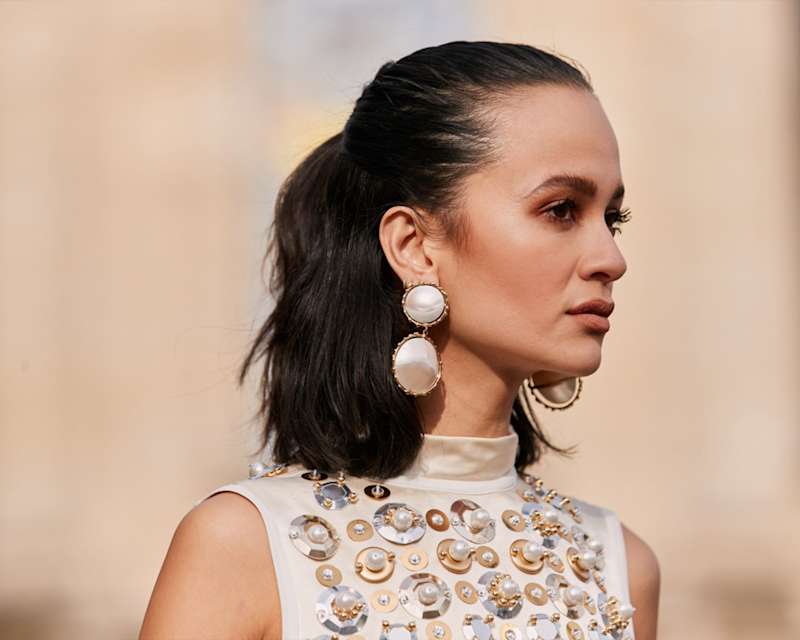 Aufnahme einer Frau im Profil mit großen Perlmutt-Ohrringen und einem hellen Top mit Applikationen bestickt