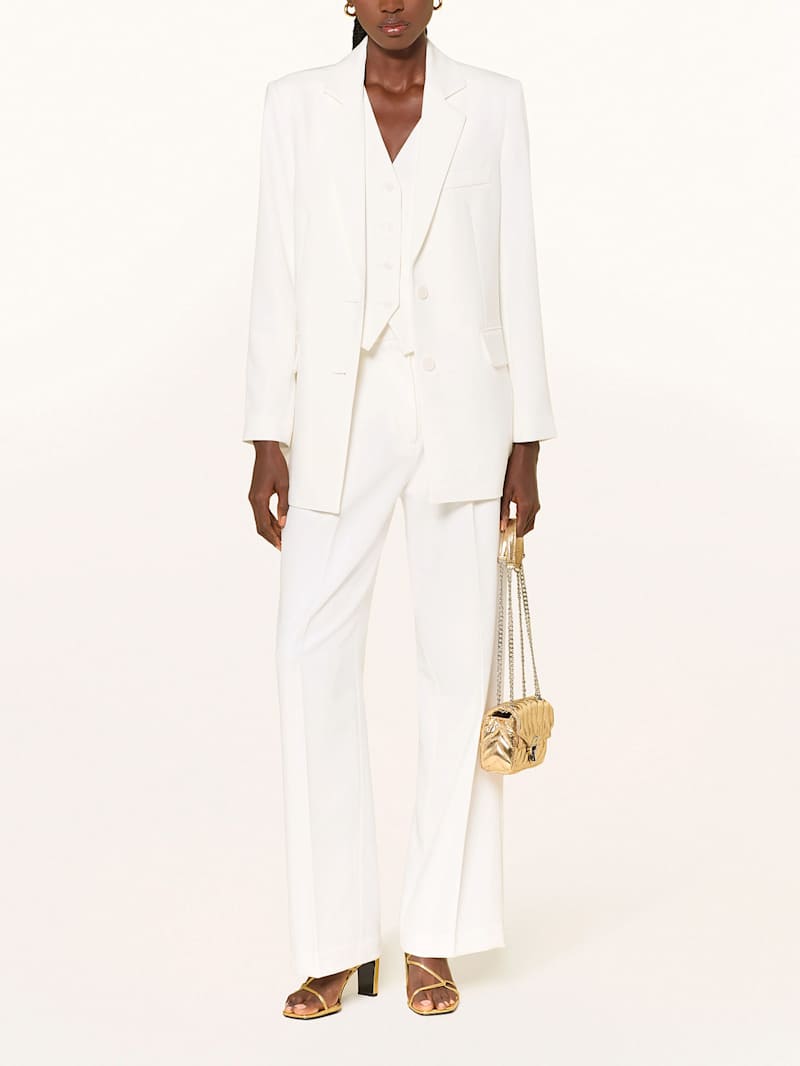 Frau trägt einen weißen Hosenanzug und dazu eine Tasche und Schuhe in der Farbe Gold