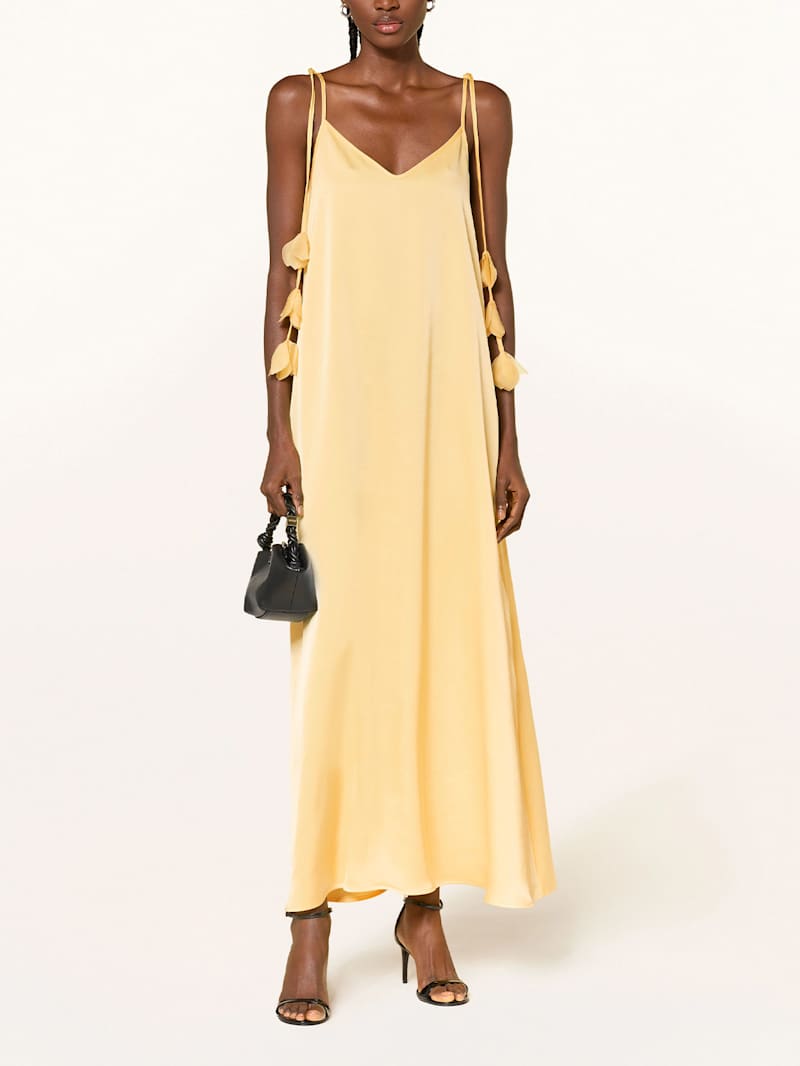 Frau trägt ein gelbes Kleid und eine schwarze Handtasche zu schwarzen High Heels