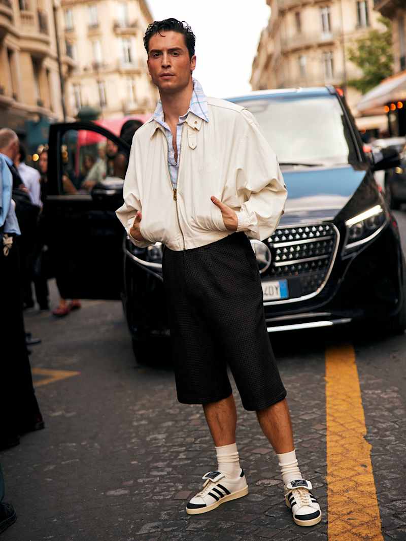 Mann trägt einen beigen Blouson zu einer schwarzen, weiten Hose und Sneaker 