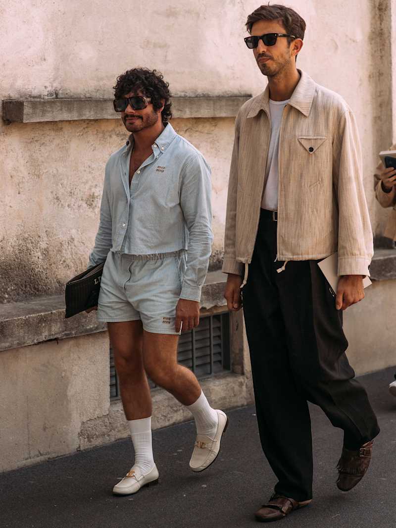 Zwei Männer gehen nebeneinander, einer trägt einen beigen Blouson, der andere Mann eine blaue Kurzjacke zur Shorts