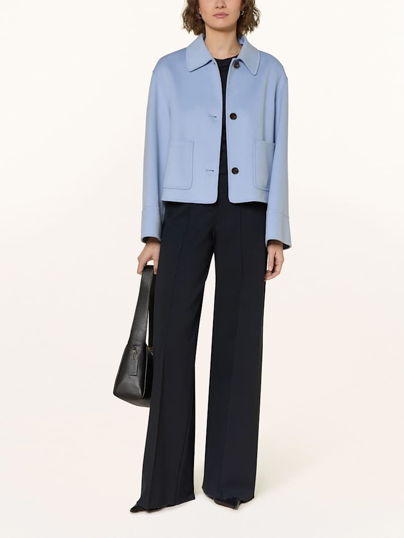 Frau stylt hellblaue Kastenjacke zu schwarzer Stoffhose und Handtasche