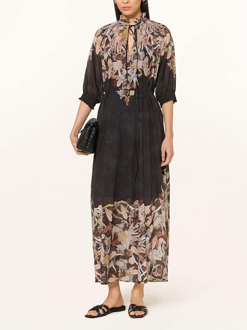 Frau trägt ein schwarzes Maxi-Kleid mit floralen Muster an Kragen und Saum