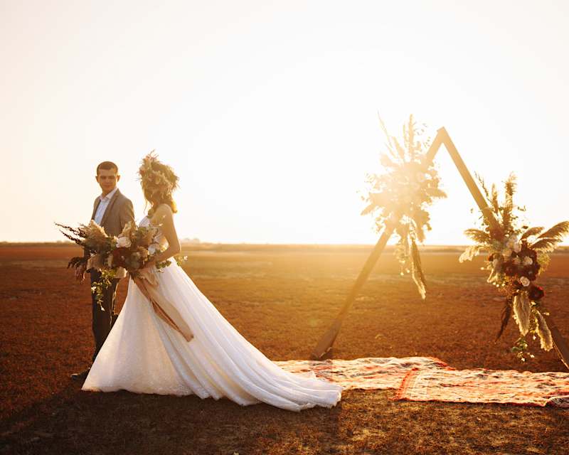 Brautpaar trägt Kleidung im Boho-Stil, im Hintergrund ist ein Sonnenuntergang