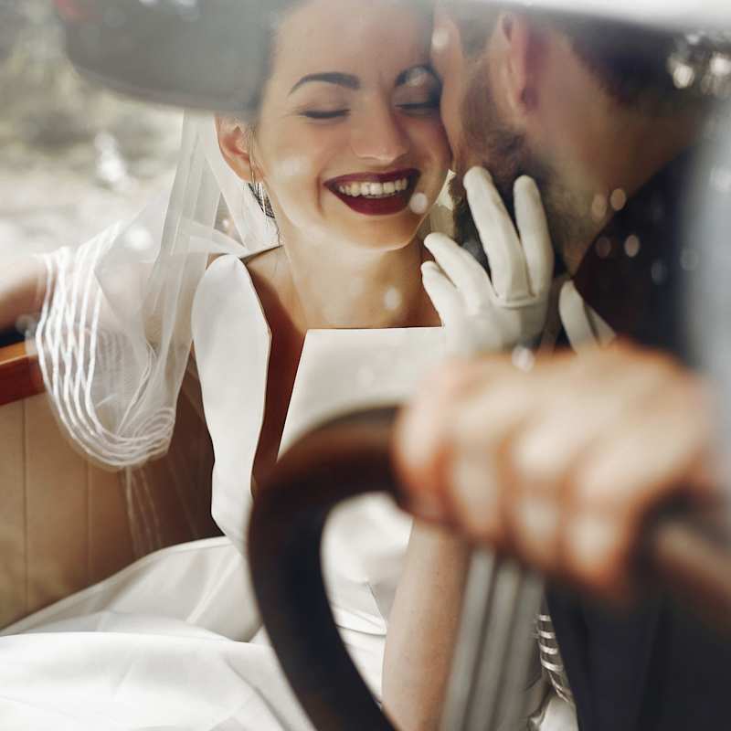 Brautpaar sitzt in einem Auto, Braut trägt ein Kleid und Make-up im Vintage-Stil