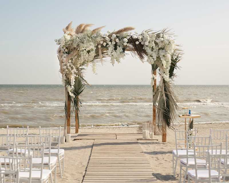 Strandhochzeit, weiße Stühle und ein Dekor-Bogenbogen
