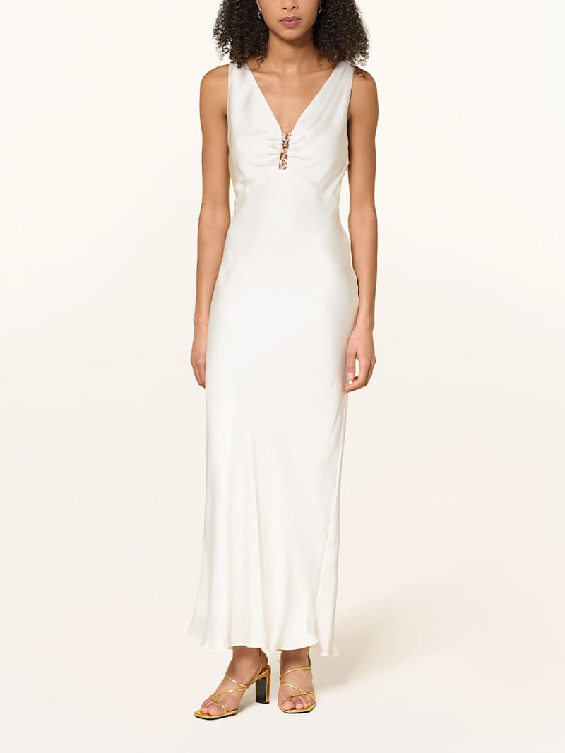 Frau trägt ein langes, weißes Satinkleid und goldene Sandalen mit Absatz