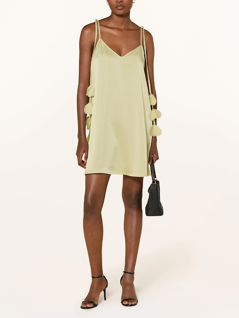 Frau trägt ein grünes Cocktailkleid, eine schwarze Handtasche und Schuhe