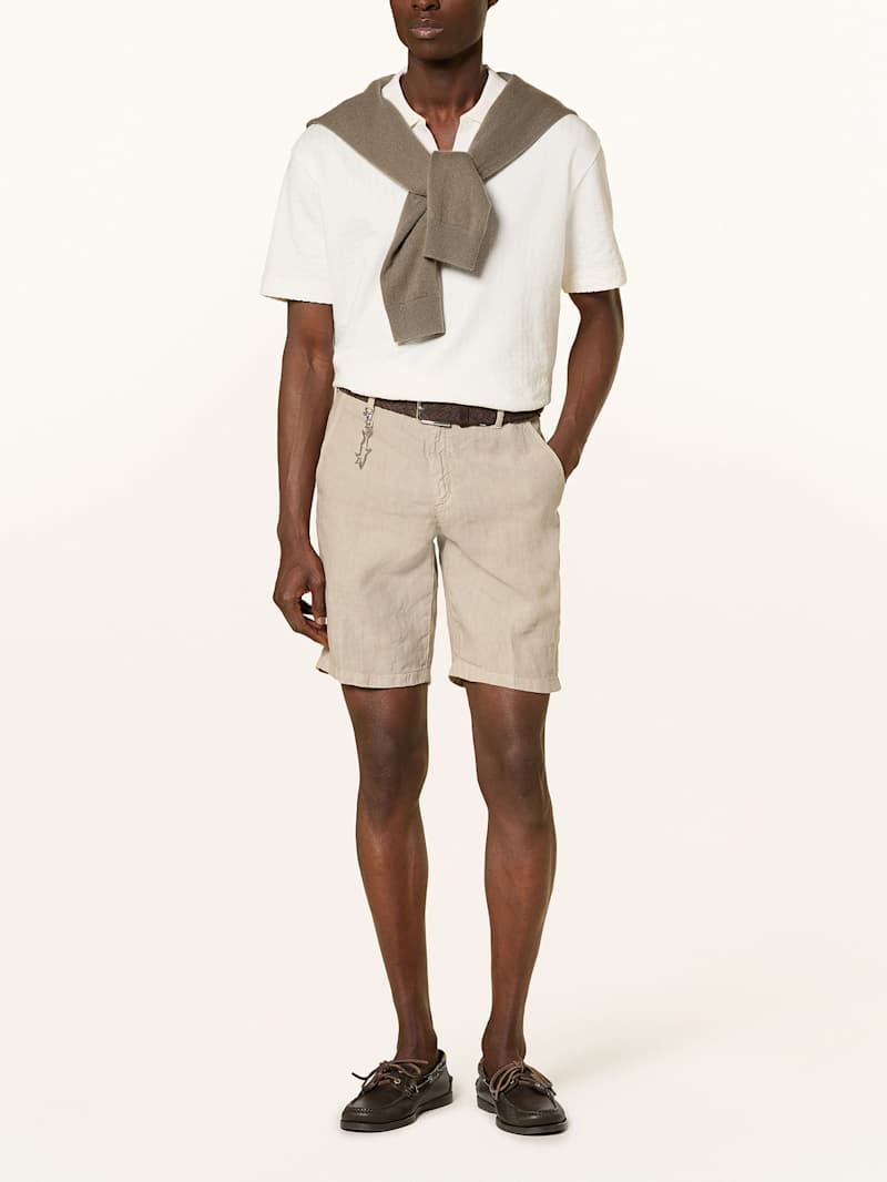 Mann trägt eine elegante beige Shorts aus Leinen zu einem off-white Poloshirt und Bootsschuhen