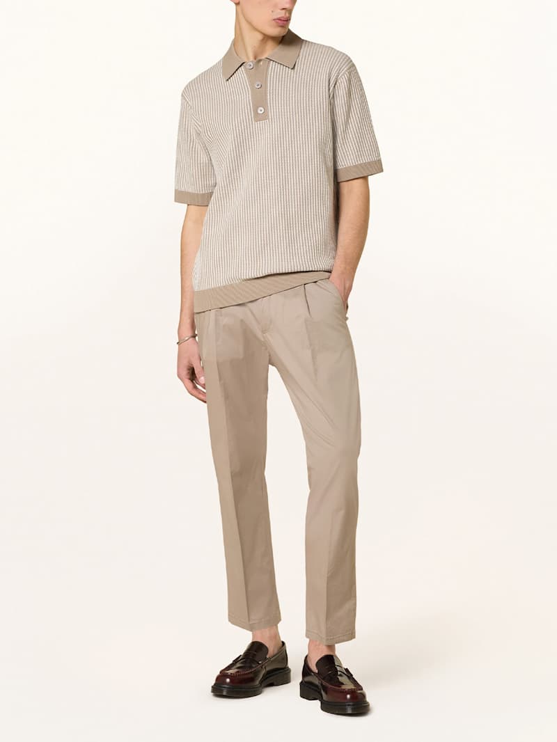 Mann trägt eine beige Hose und ein Strick-Shirt in Cremebeige, dazu dunkelbraune Loafer