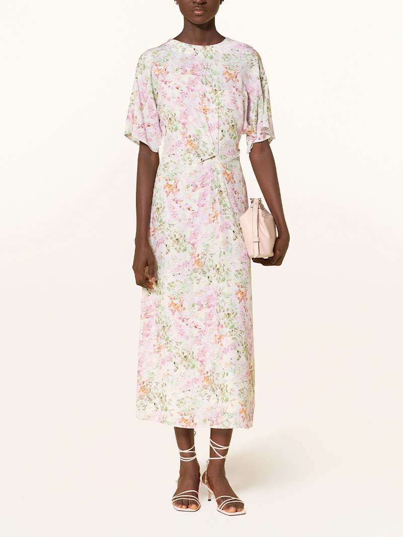 Frau trägt ein leicht tailliertes, langes Kleid mit kurzen Ärmeln und floralen Muster