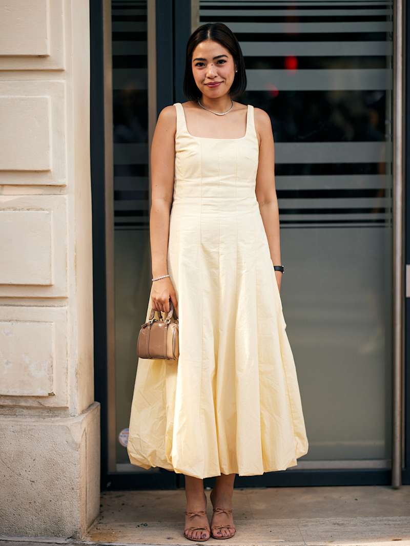 Brunetka w jasnożółtej sukience z małą brązową torebką i w pasujących sandałkach