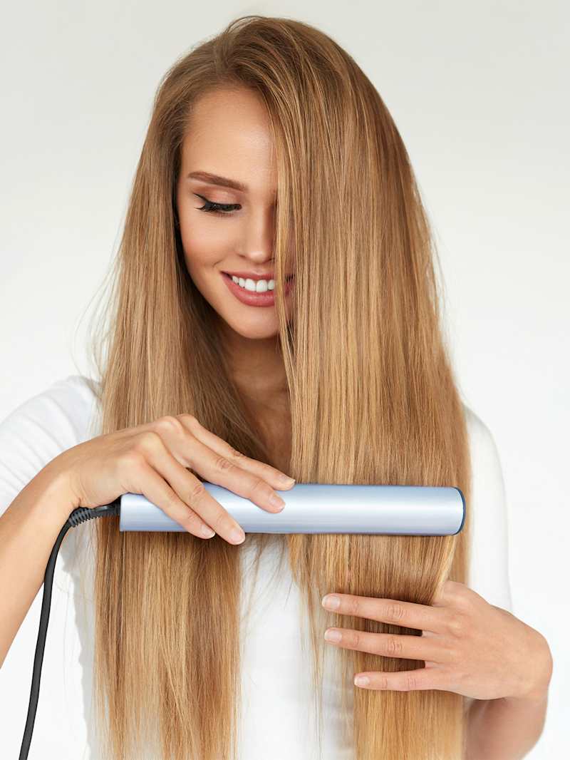 Frau stylt sich die Haare mit einem Glätteisen