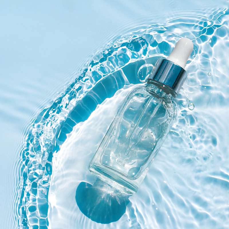 Serum-Flasche auf einem wasserbettähnlichen Untergrund vor blauem Hintergrund