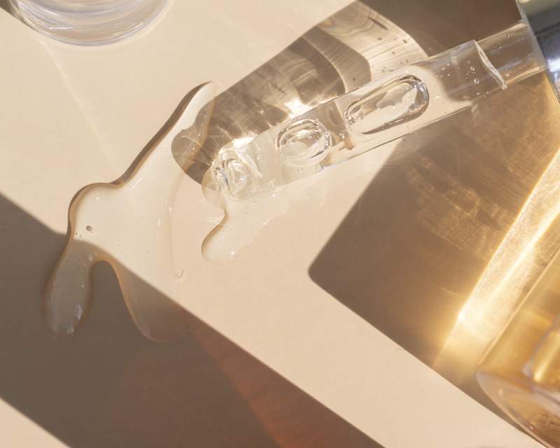 Eine Pipette eines Serum-Fläschchens liegt auf einem beigen Untergrund, es befindet sich eine Flüssigkeit auf der Fläche