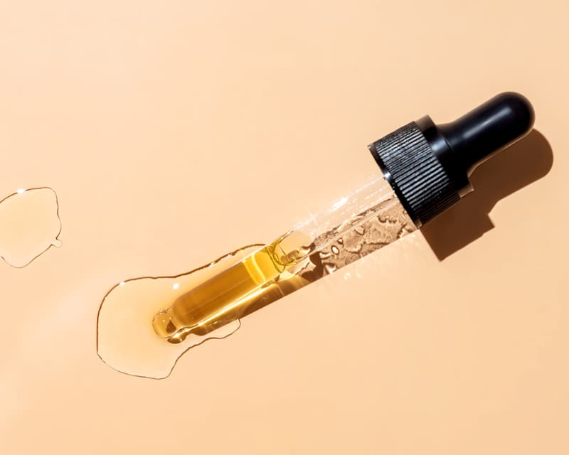 Retinol-Serum tropft aus Pipette auf hellorangem Hintergrund.
