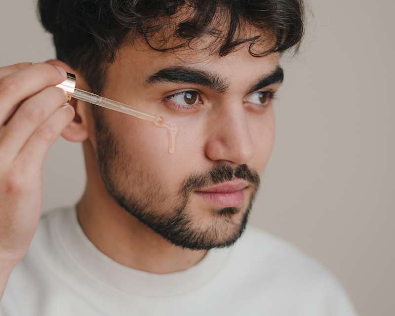 Mann trägt sich mit einer Pipette Serum auf die untere Augenpartie und Wange auf