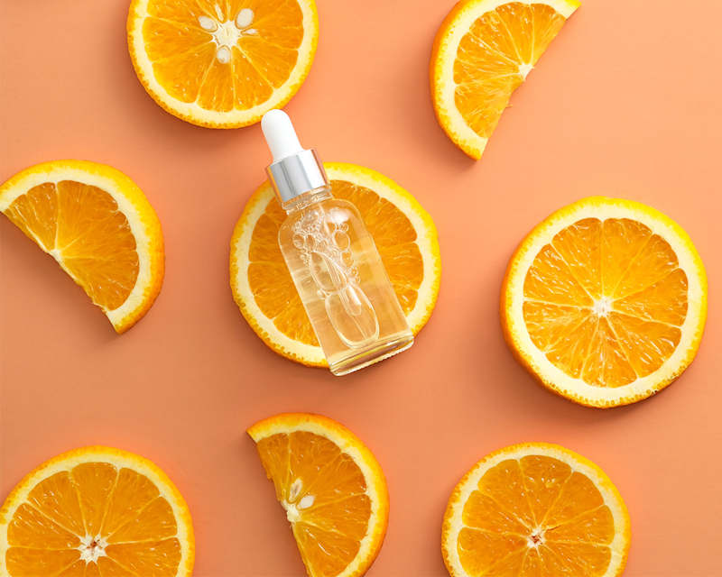 Vitamin-C-Serum für die Hautpflege zwischen Orangenscheiben auf orangefarbenem Hintergrund