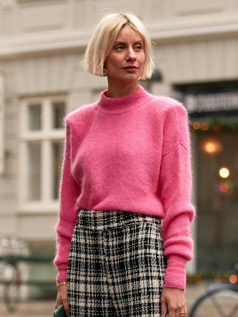 Frau mit einem blonden Blunt Cut trägt einen pinken Pullover zu einer karierten Hose