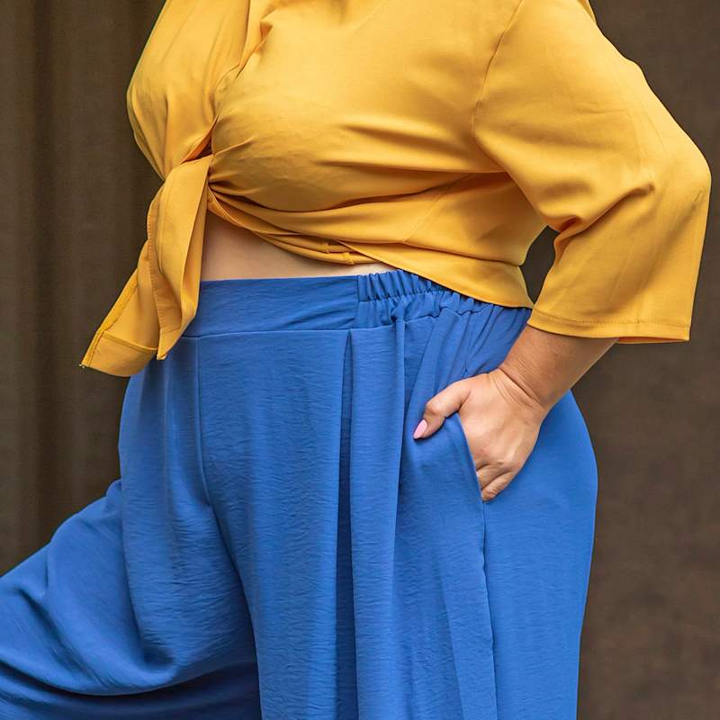 Nahaufnahme einer Frau in gelber Bluse und blauer Hose mit bequemem Taillenbund und weit geschnittenen Beinen