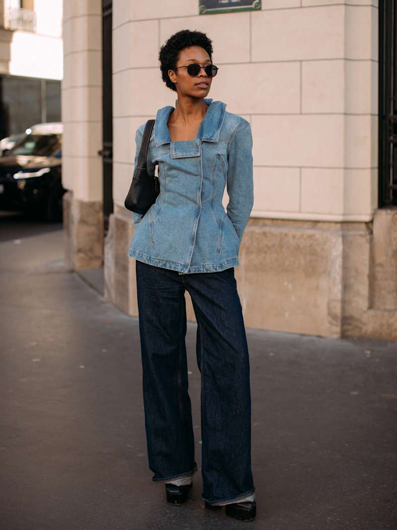 Frau trägt eine helle Jeansjacke zu einer dunklen Indigo-Denim, dazu eine Sonnenbrille und schwarte Boots.