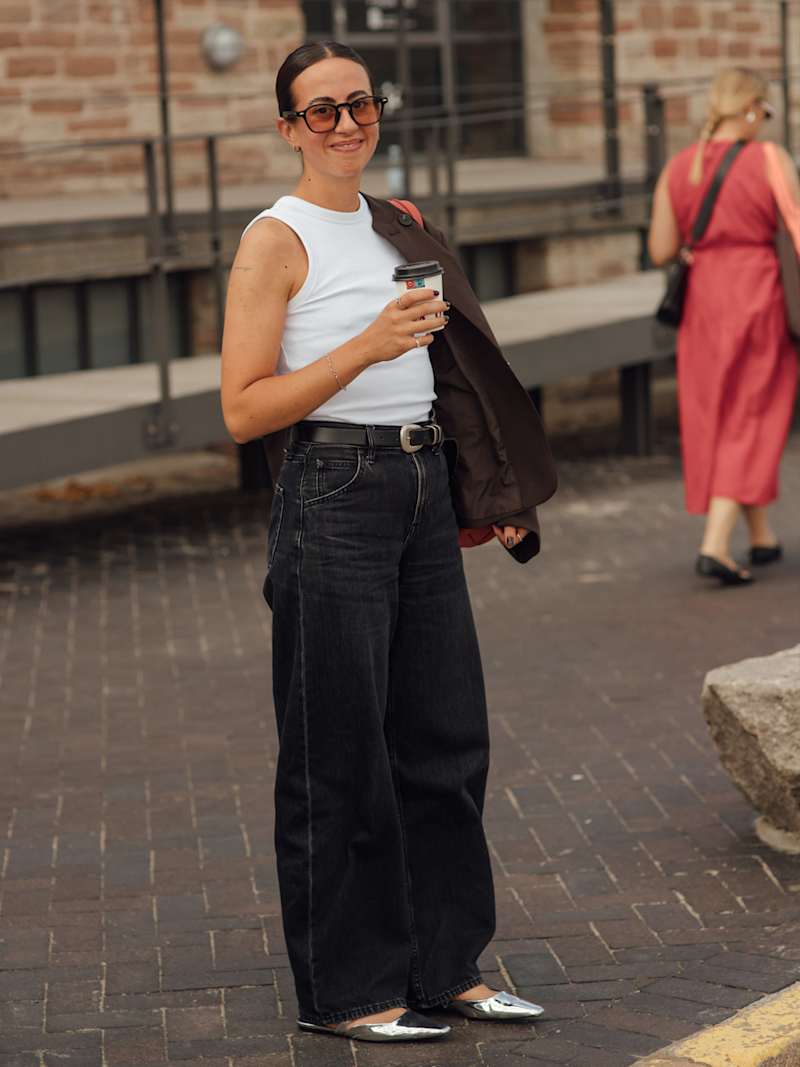 Frau trägt eine Wide-Leg-Jeans in der Farbe Grau, dazu ein weißes Top und silberne Schuhe.