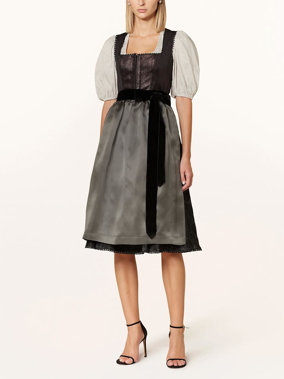 Blonde Frau trägt schwarzes Dirndl mit Glitzer und grauer Schürze