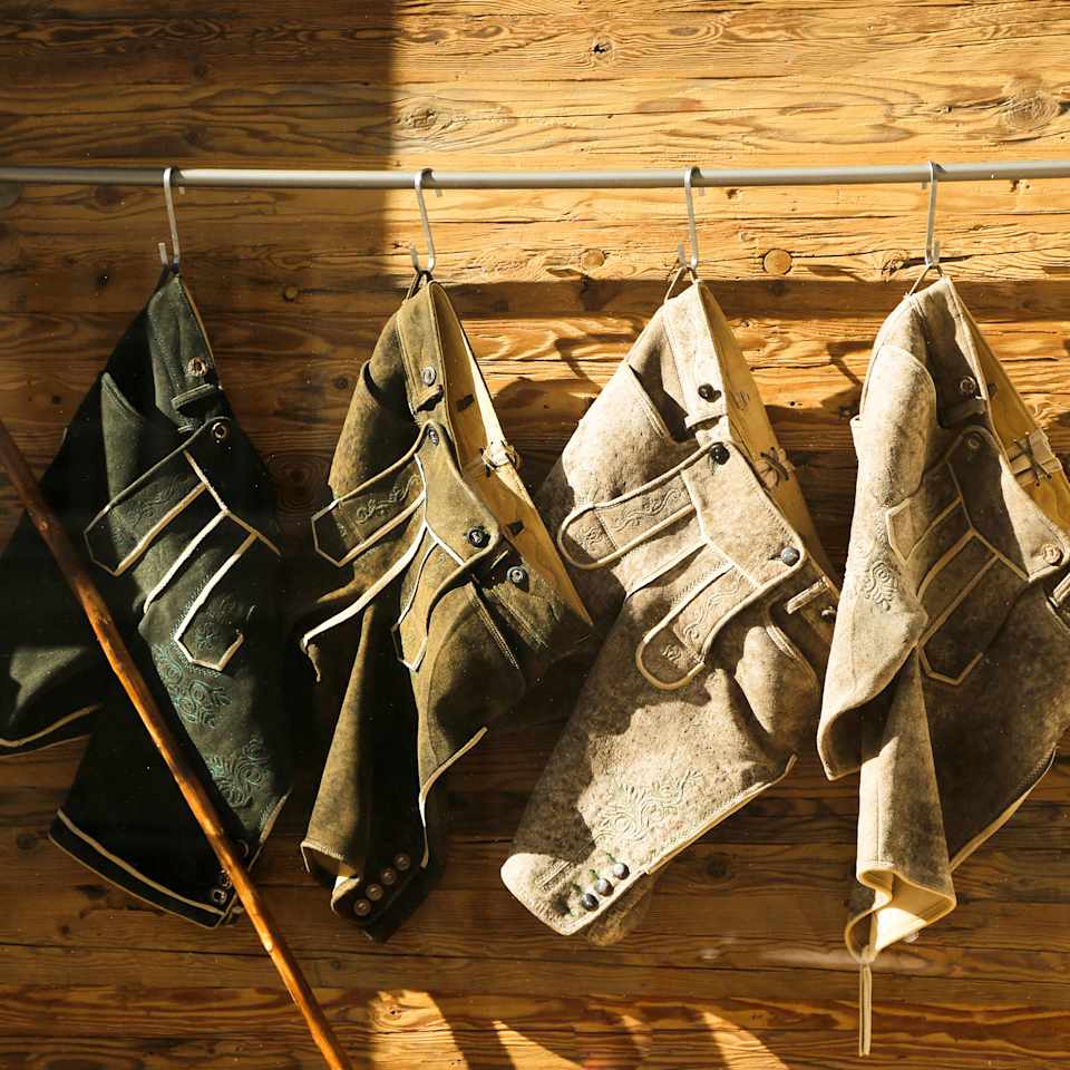 Vier Lederhosen in unterschiedlichen Farben hängen an einer Kleiderstange