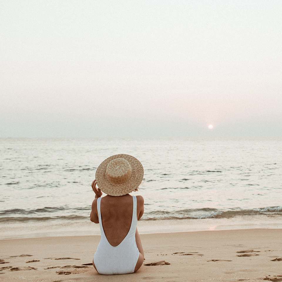 Frau in einem weißen Badeanzug sitzt am Strand 