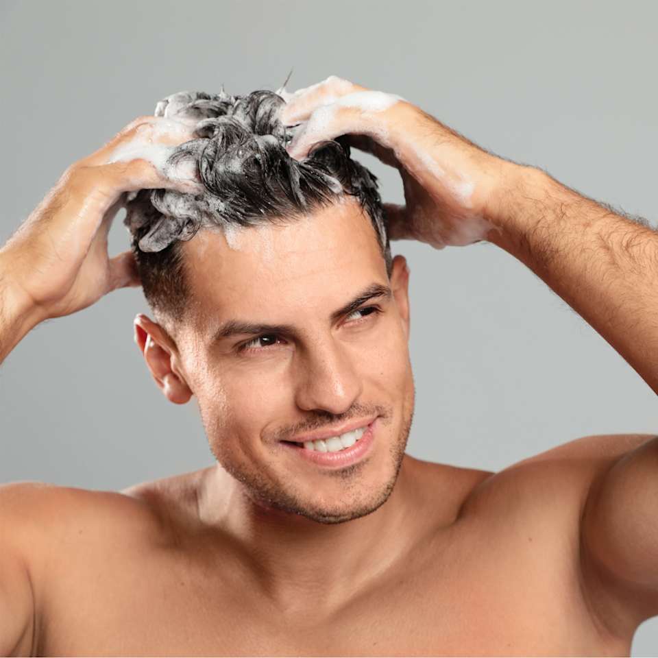 Brünetter Mann wäscht sich die Haare mit Shampoo