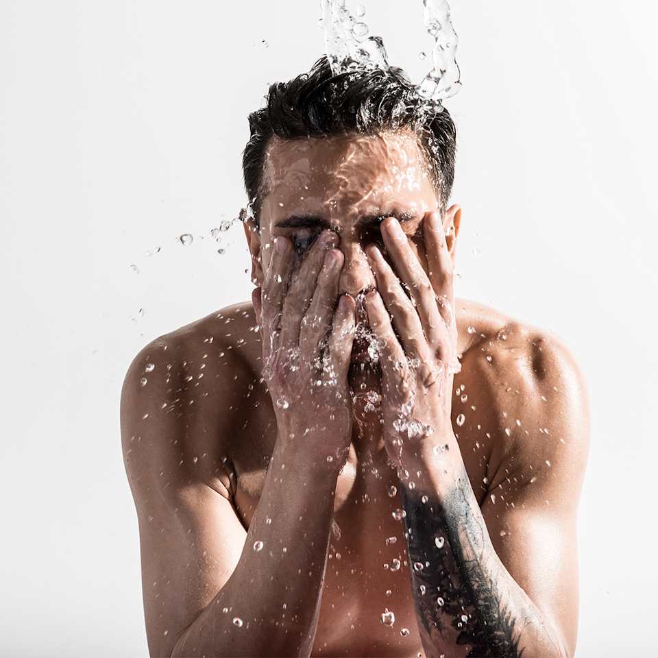 Mann mit dunklen Haaren wäscht sich das Gesicht mit Wasser