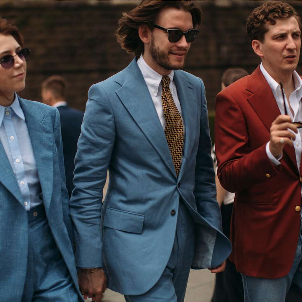 Eine Frau und zwei Männer tragen Anzüge in den Farben Blau und Rot