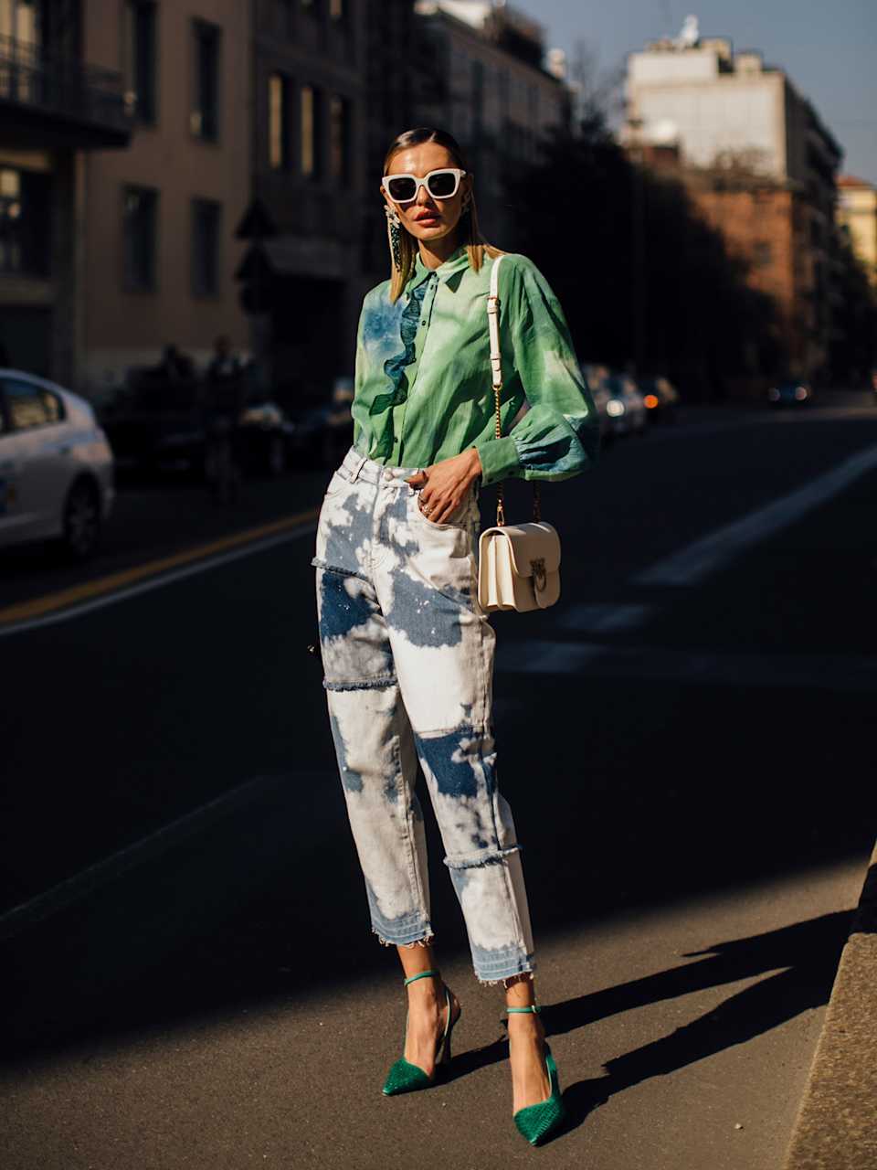 Elegant gekleidete Frau in Batikhosen und grünem Hemd zu grünen Pumps trägt weiße Handtasche über die Schulter.