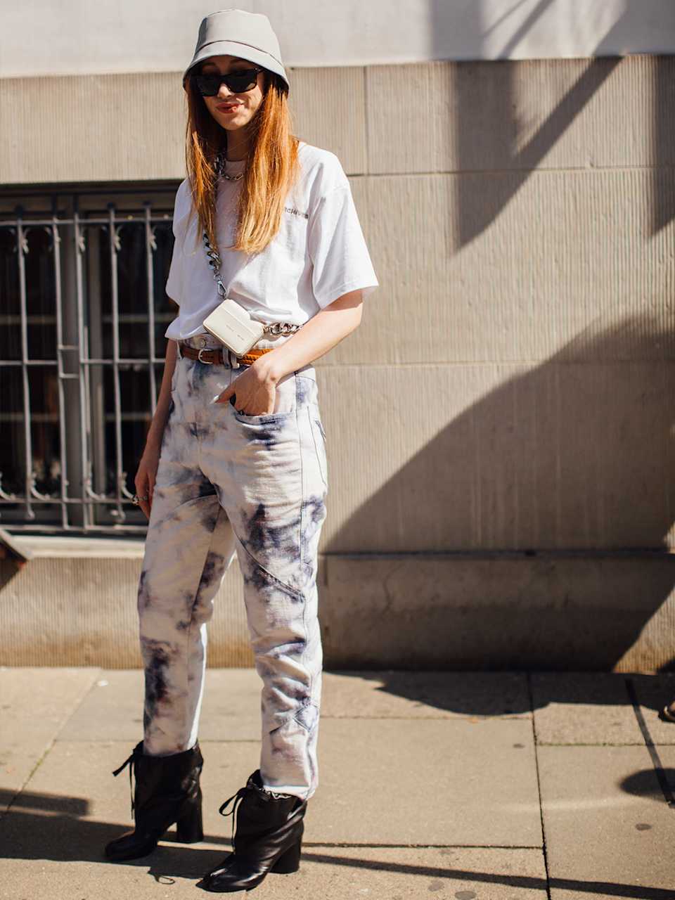 Frau trägt Hose mit Batik-Muster zu weißem T-Shirt und schwarzen Stiefeletten, dazu ein Bucket-Hat.