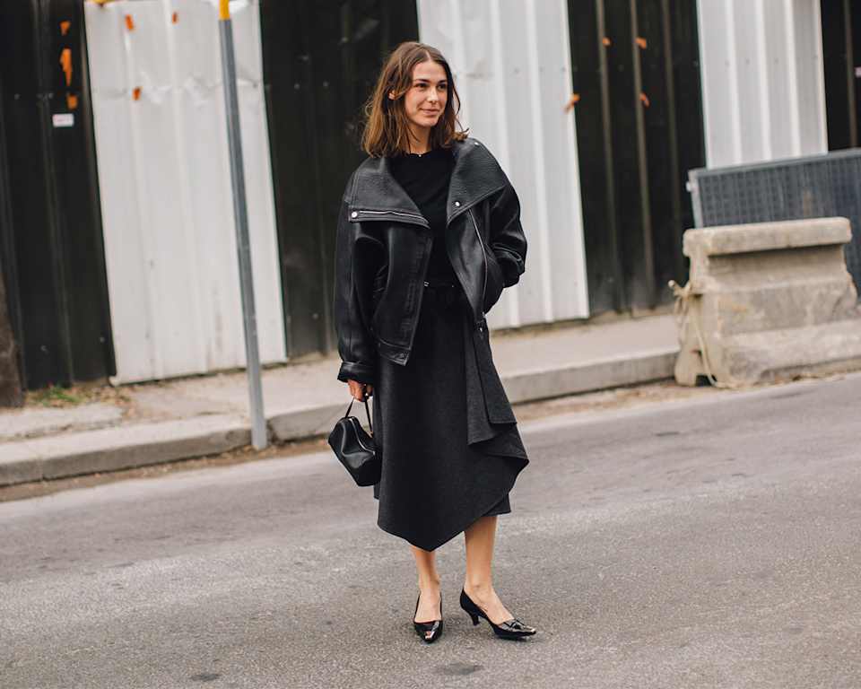 Brünette Frau kombiniert schwarze Oversized-Lederjacke mit schwarzem Midi-Kleid und Pumps