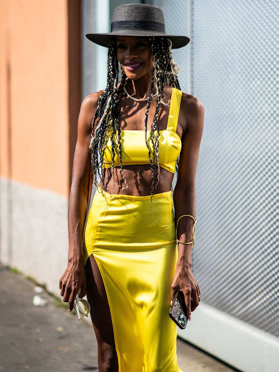 Frau trägt einen schwarzen Hut zu einem Set bestehend aus gelben Bustier und Rock 