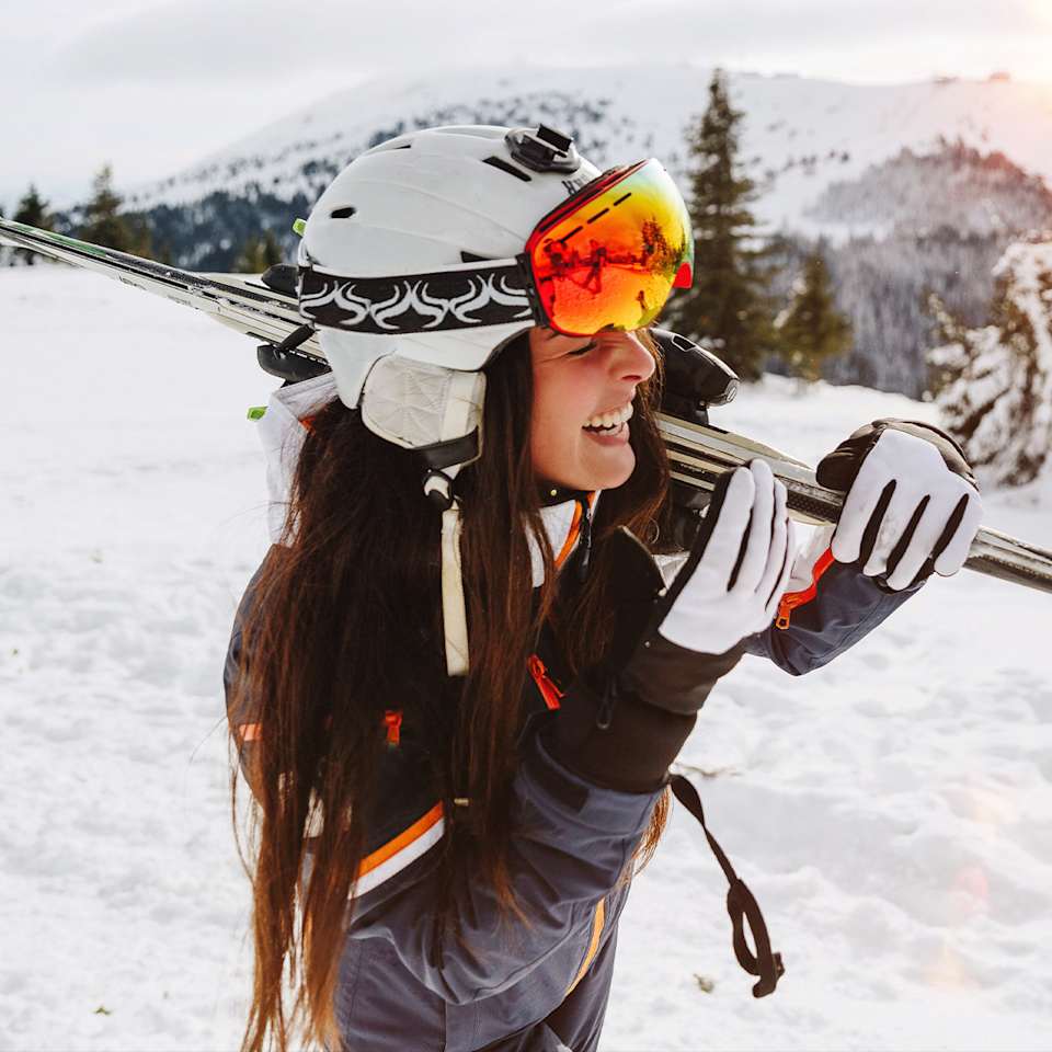 Frau in Skibekleidung trägt Skier auf der Schulter