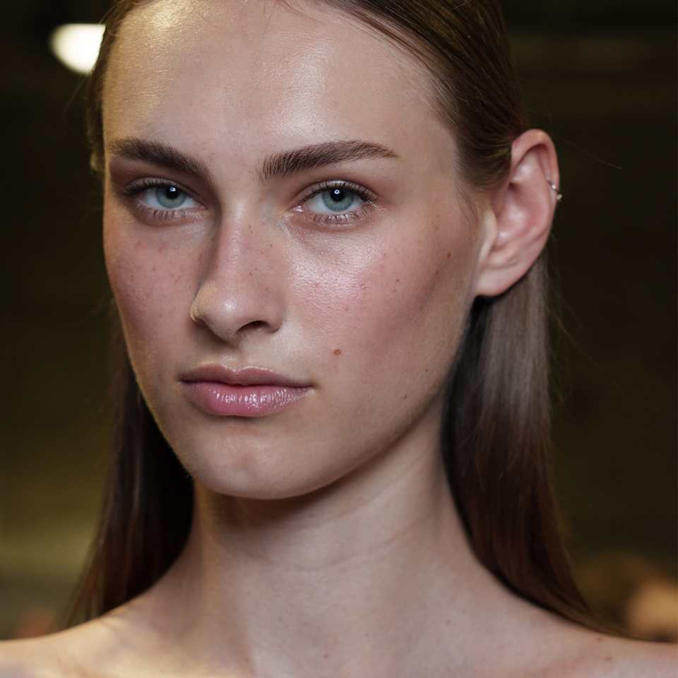 Dunkelblonde Frau mit natürlichem Glow-Make-up, betonten Brauen und Gloss-Lippen