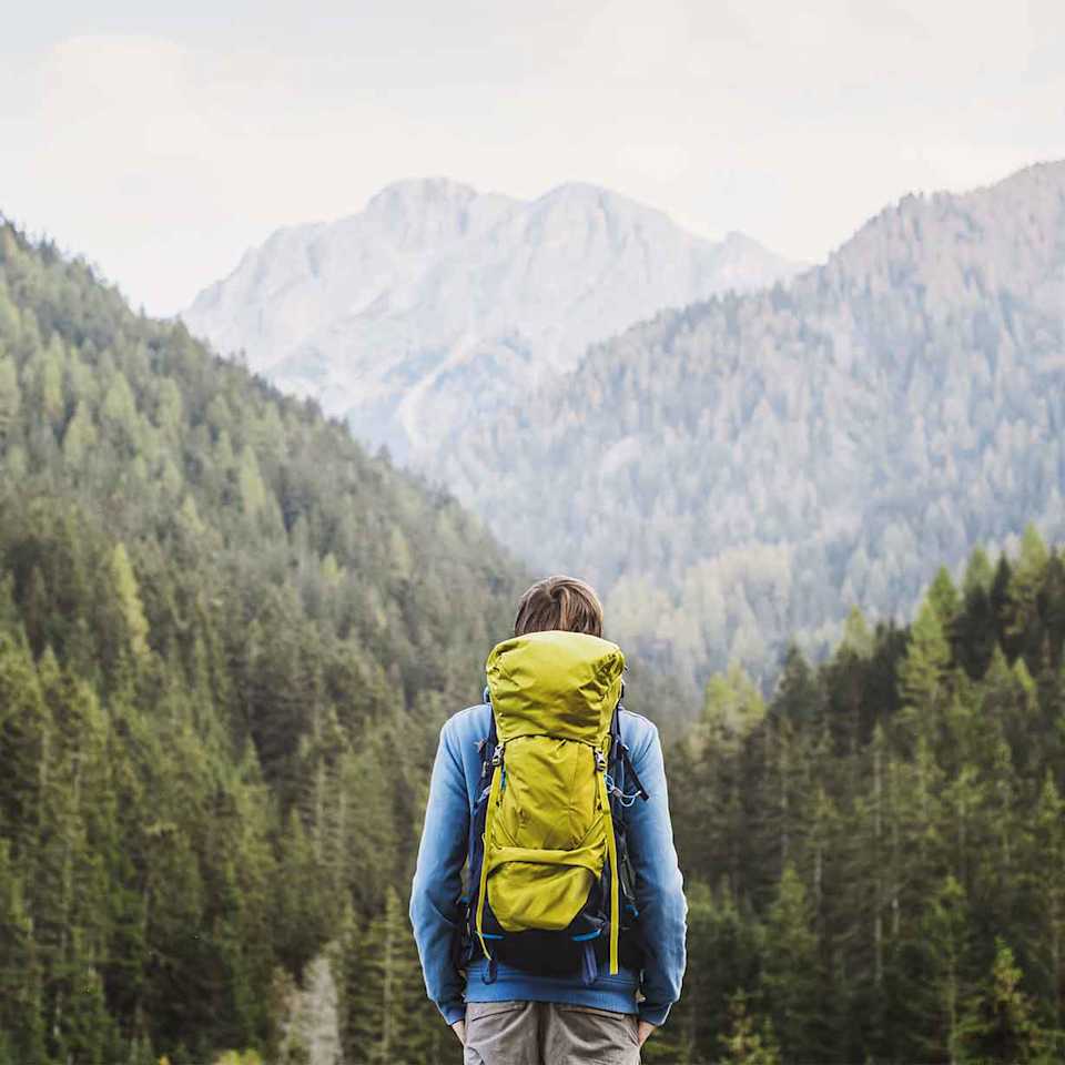Person steht vor einem Berg beim Wandern und trägt einen grünen Wanderrucksack