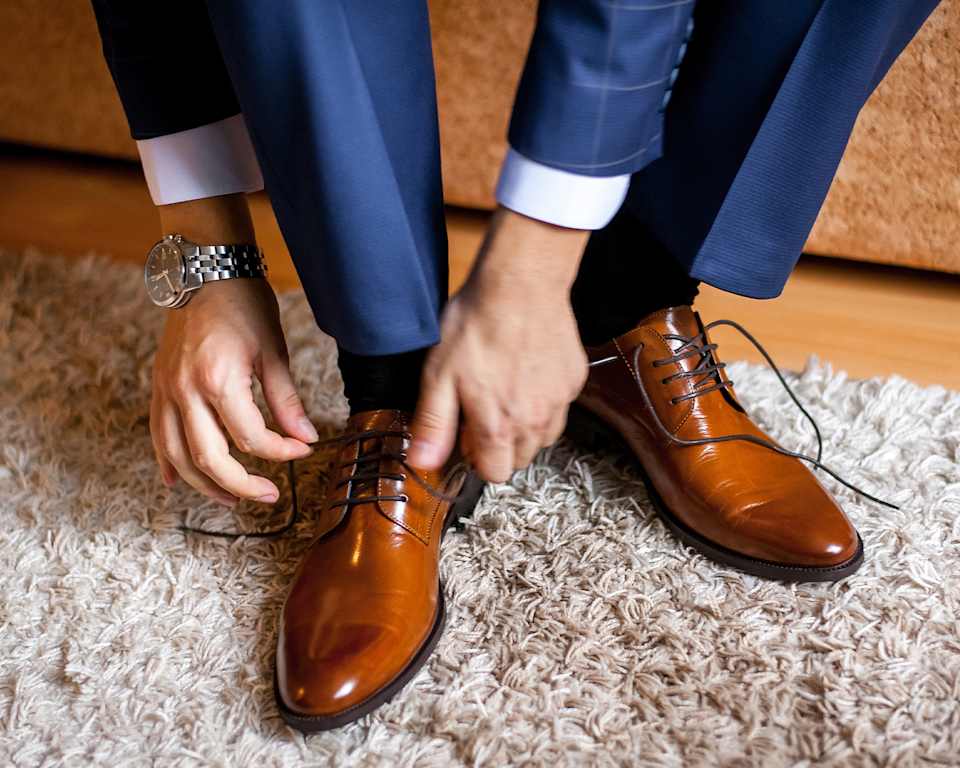Mann im Anzug bindet sich seine braunen Schnürschuhe zu