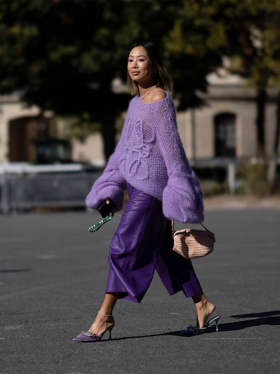Frau in schwarzen Mules trägt lila Outfit zu beiger Handtasche