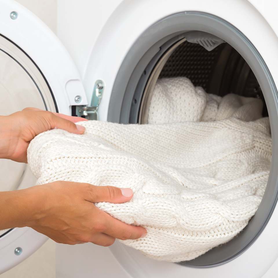 Weißer Wollpullover wird aus der Waschmaschine genommen