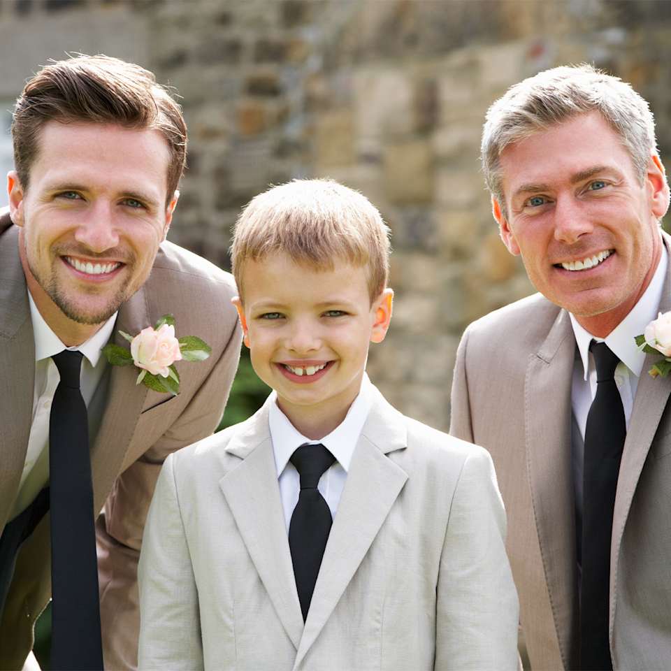Ein Junge steht in der Mitte von zwei Männern, alle tragen graue Hochzeits-Anzüge
