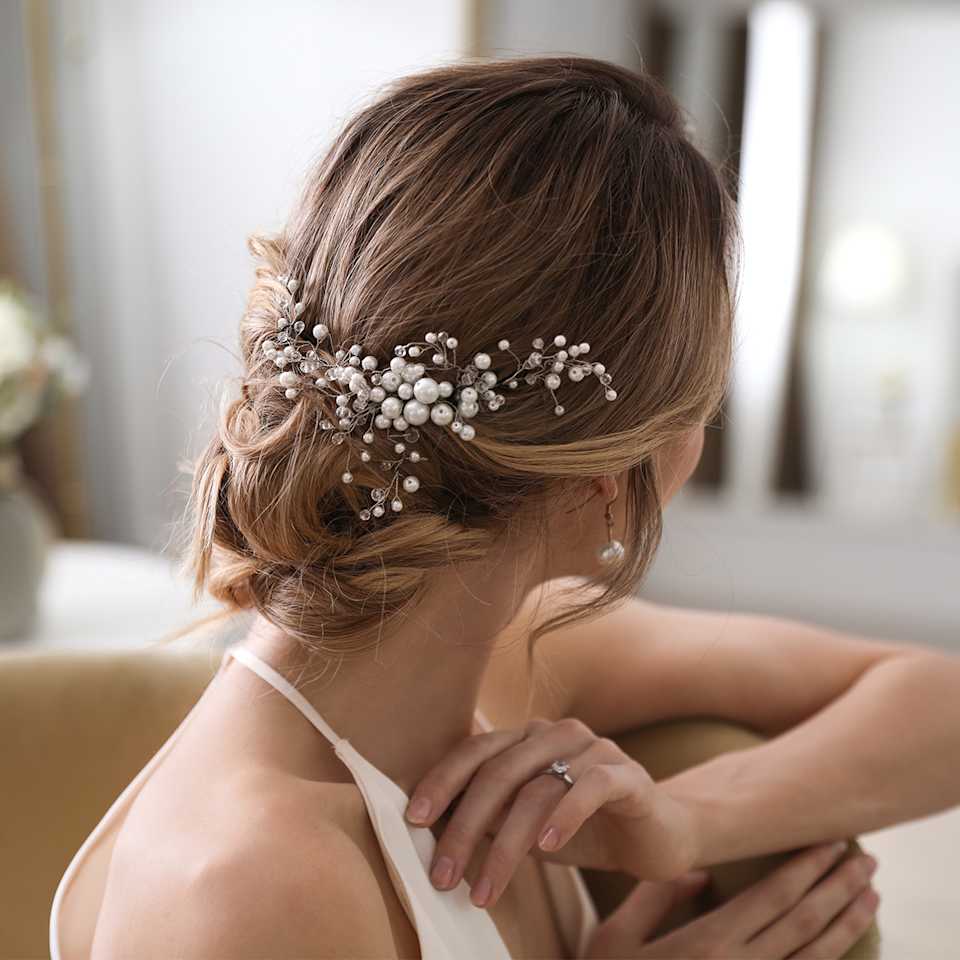 Braut vor einem Spiegel mit Hochsteckfrisur und Blüten im Haar