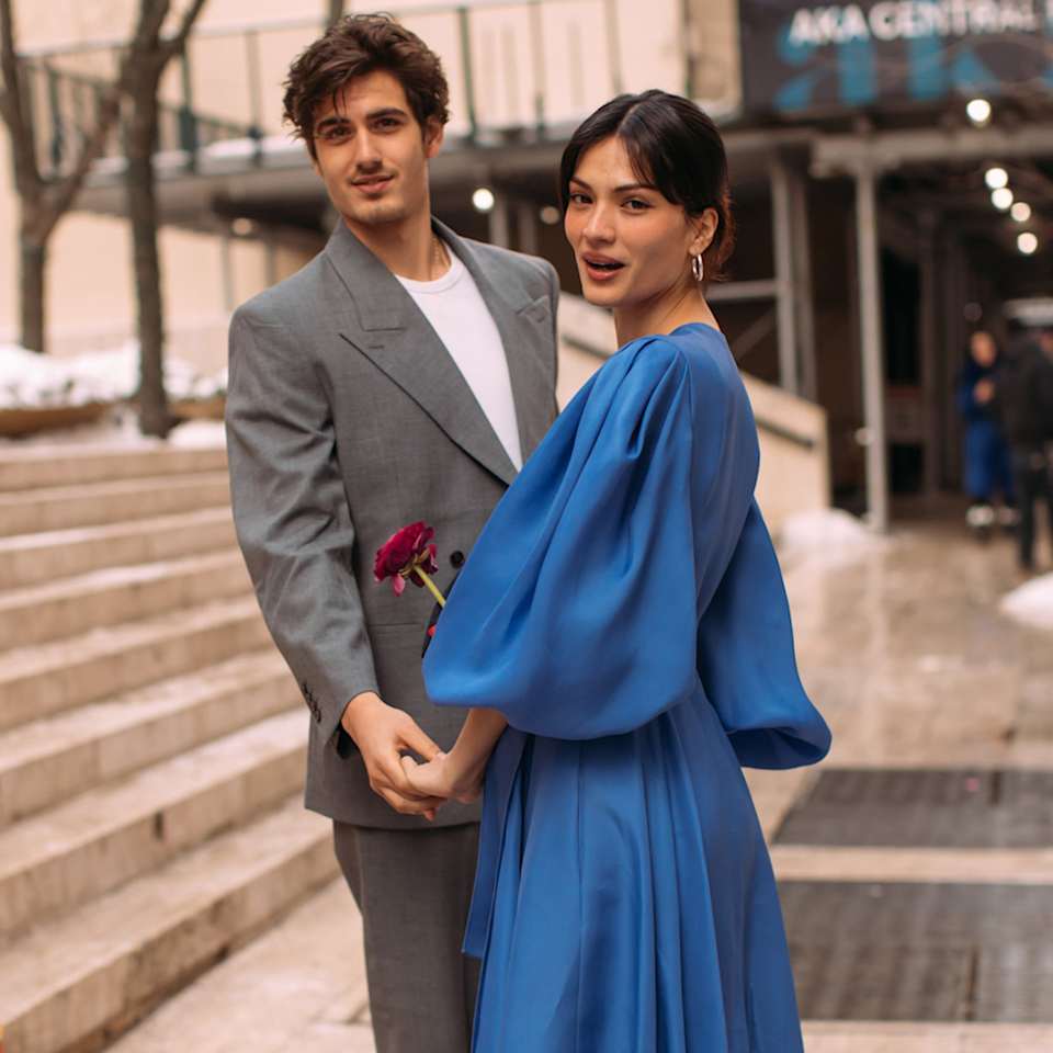 Ein Mann im grauen Anzug und eine Frau in einem blauen Kleid halten sich an den Händen