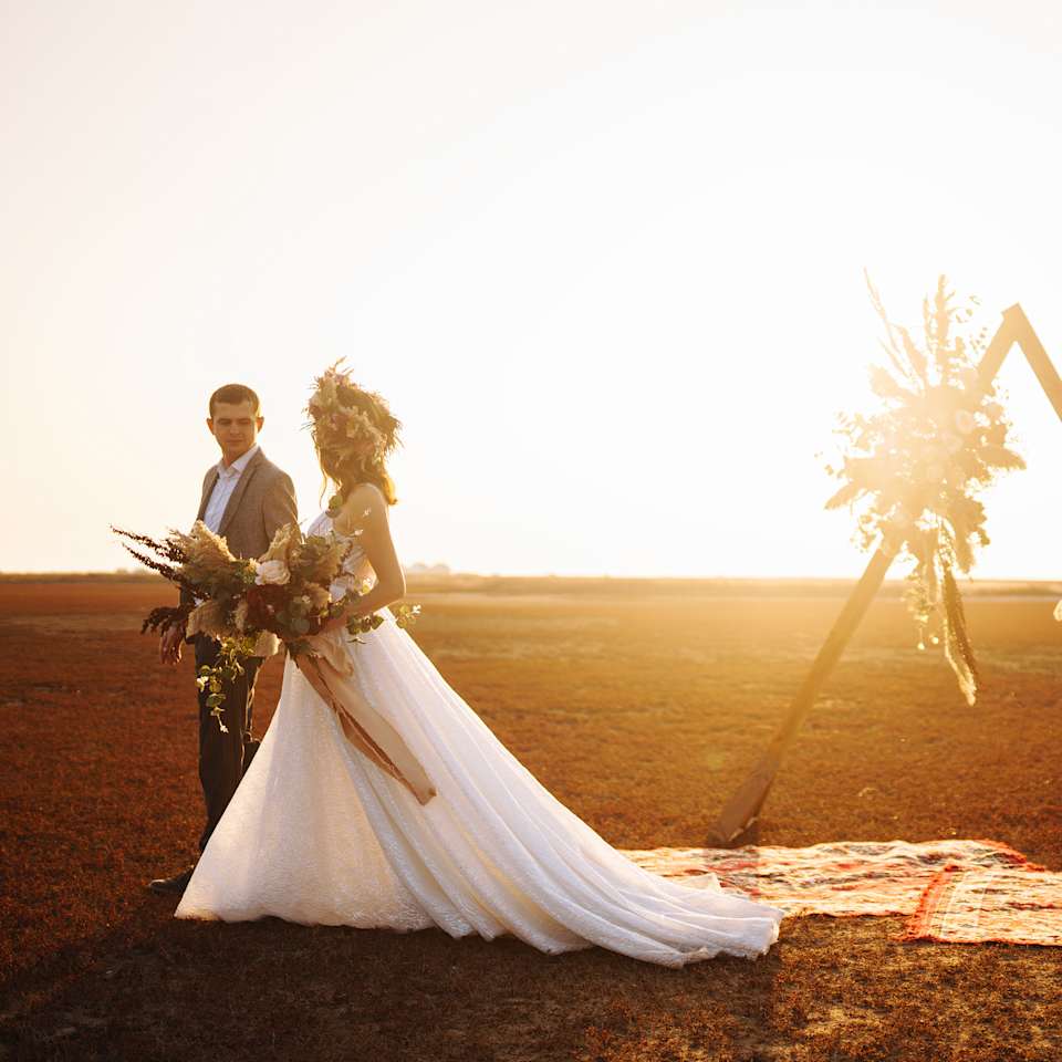 Hochzeitspaar steht während eines Sonnenuntergangs auf einer Wiese